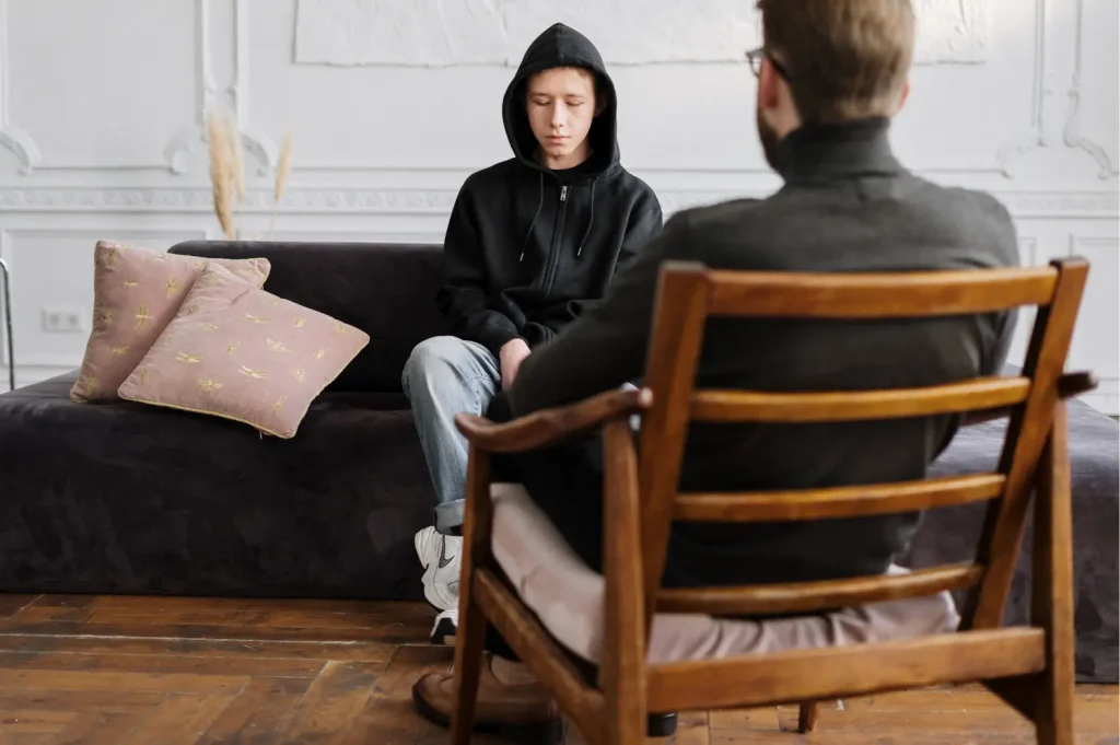 rehab inpatient program featuring a teen in a hoodie speaking with a therapist in a calm office setting