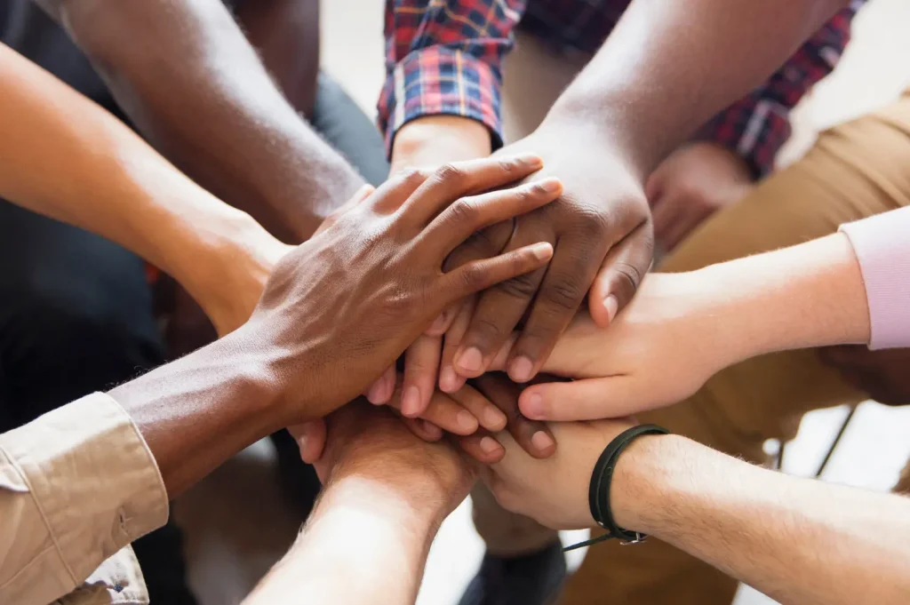 Substance abuse help group members showing unity with hands stacked in a supportive gesture.