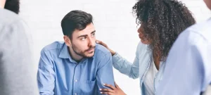Substance abuse help group member offering support to a distressed man during a counseling session.