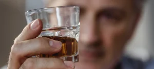 Substance abuse program concept with man staring thoughtfully at a glass of alcohol.