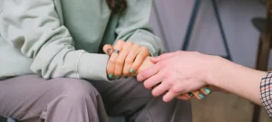Accredited rehab centers support session showing close-up of two people holding hands during emotional recovery.