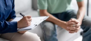 Addiction recovery programs session with counselor taking notes during a therapy meeting with a patient on a couch.