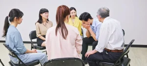 Depression treatment centers group therapy session with individuals offering emotional support to a distressed man in a circle.