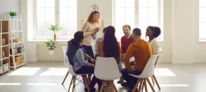 Drug rehabilitation center group session with adults sharing personal experiences in a bright, supportive environment.