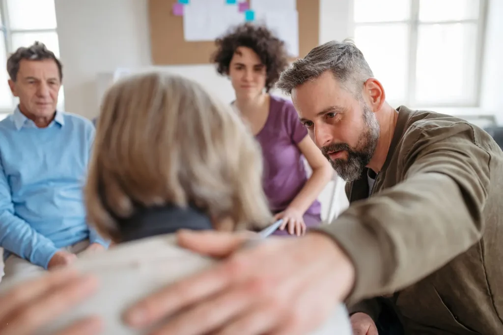 Private rehab facilities support group where a man gently comforts a woman, showing empathy in a therapeutic environment.