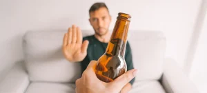 Sober coaching programs support man refusing alcohol with a hand gesture while sitting on a couch.