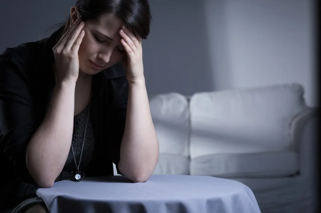 Woman sits alone with hands on her temples, showing anxiety, depression, or overwhelm.