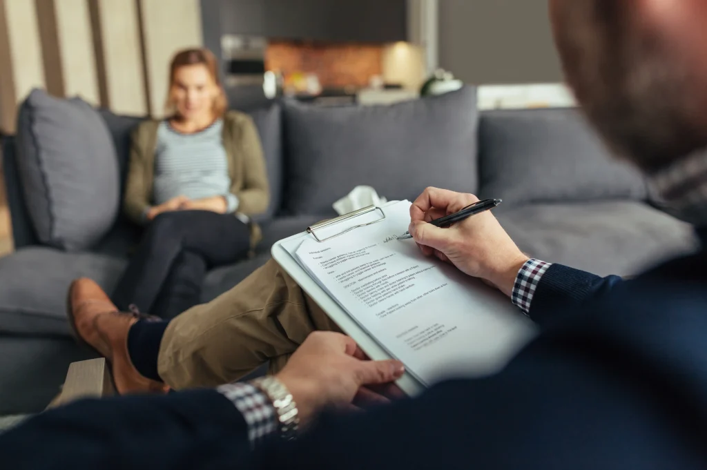 Benefits of hiring a recovery coach illustrated by a counselor taking notes while a client speaks, highlighting personalized accountability and support.