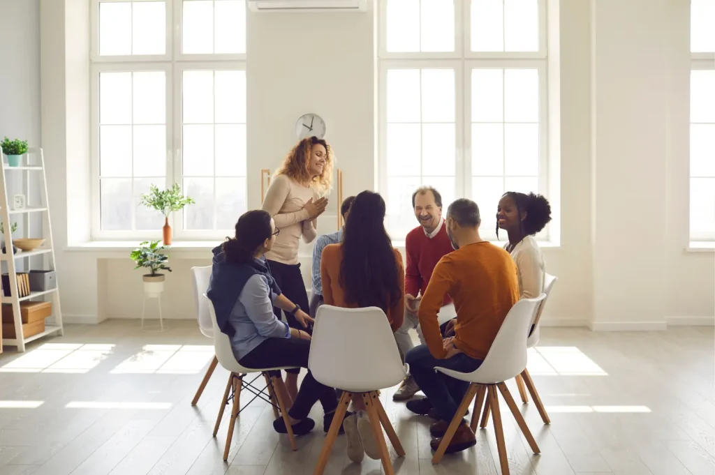 How to choose a rehab facility illustrated by a supportive group therapy meeting in a bright room with participants in discussion.