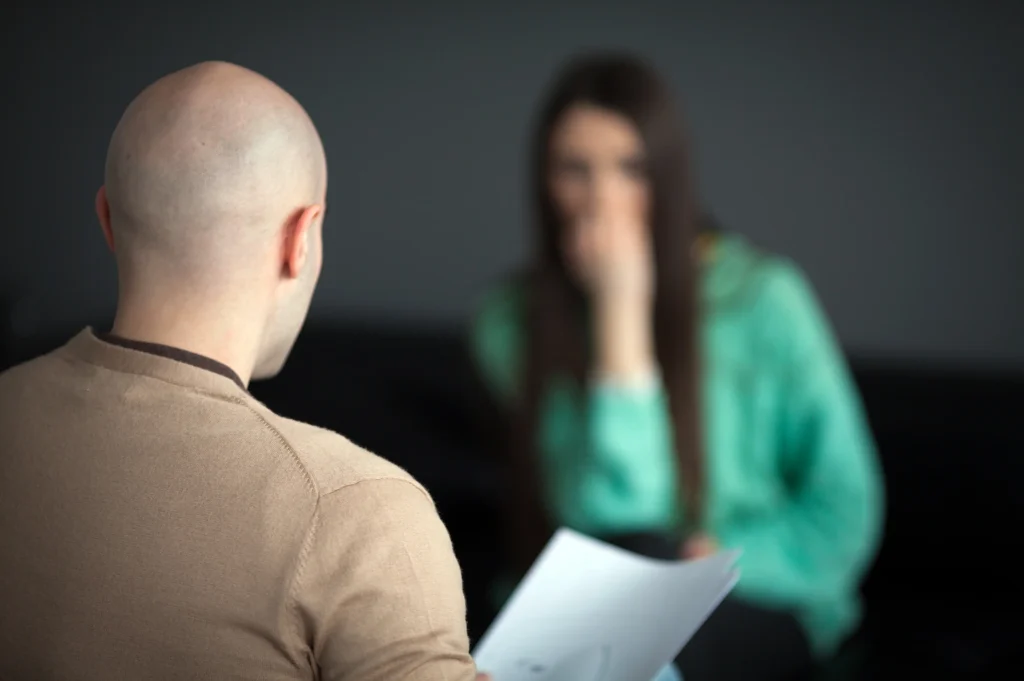 Questions before entering rehab discussed during an intake-style meeting with a counselor taking notes.