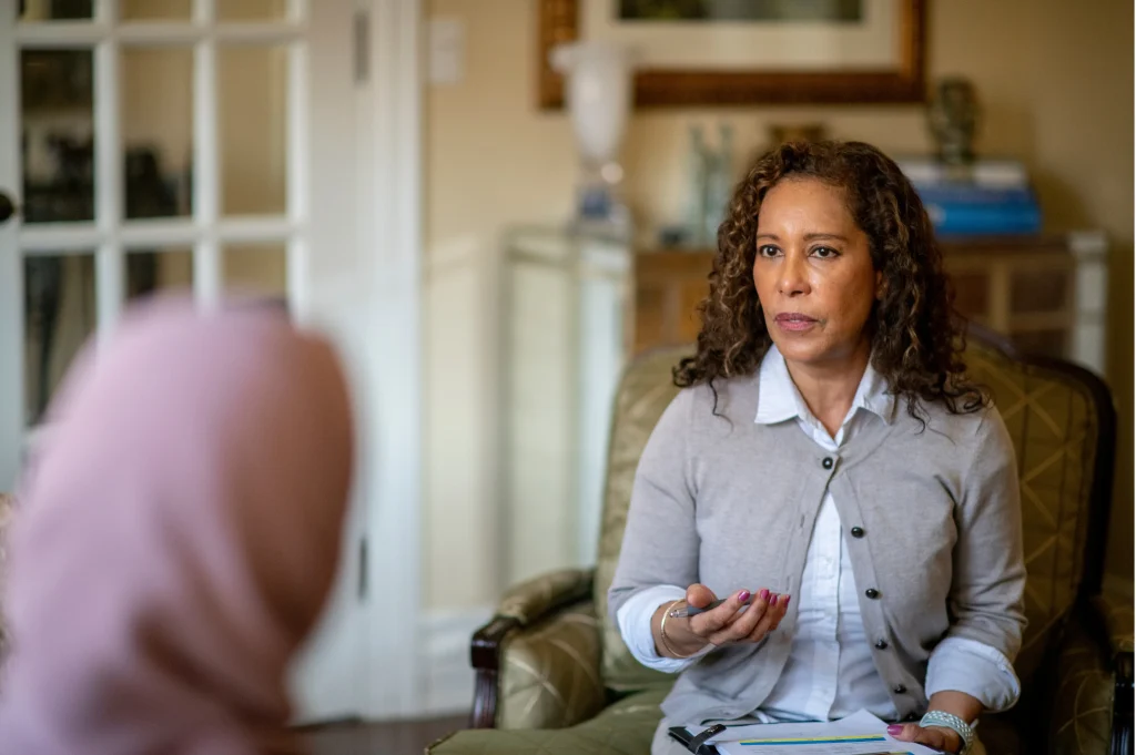 a recovery coach depicted as a one-on-one coaching session with a professional holding notes and listening to a client at home.