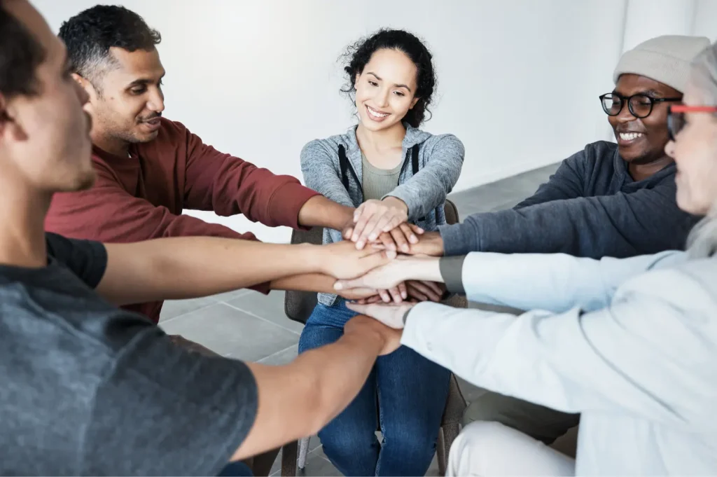 Sober living communities depicted as a diverse group placing hands together in unity during a recovery support circle.