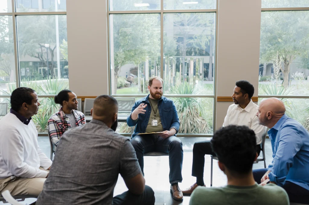 sobriety coaches showing a support group meeting in a bright room with a facilitator guiding participants in discussion.