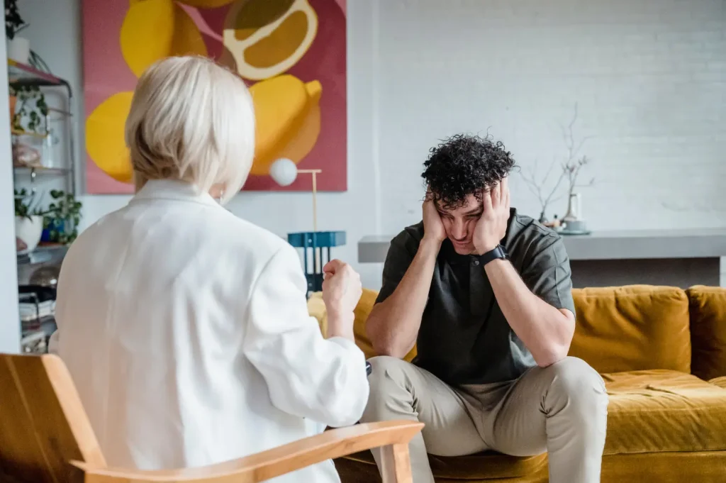 Ways to afford addiction treatment explored in a counseling session as a distressed man speaks with a therapist on a couch.