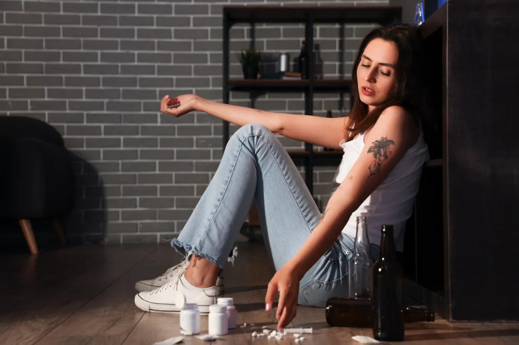 woman on floor surrounded by pills and bottles showing visible signs of needing addiction recovery support