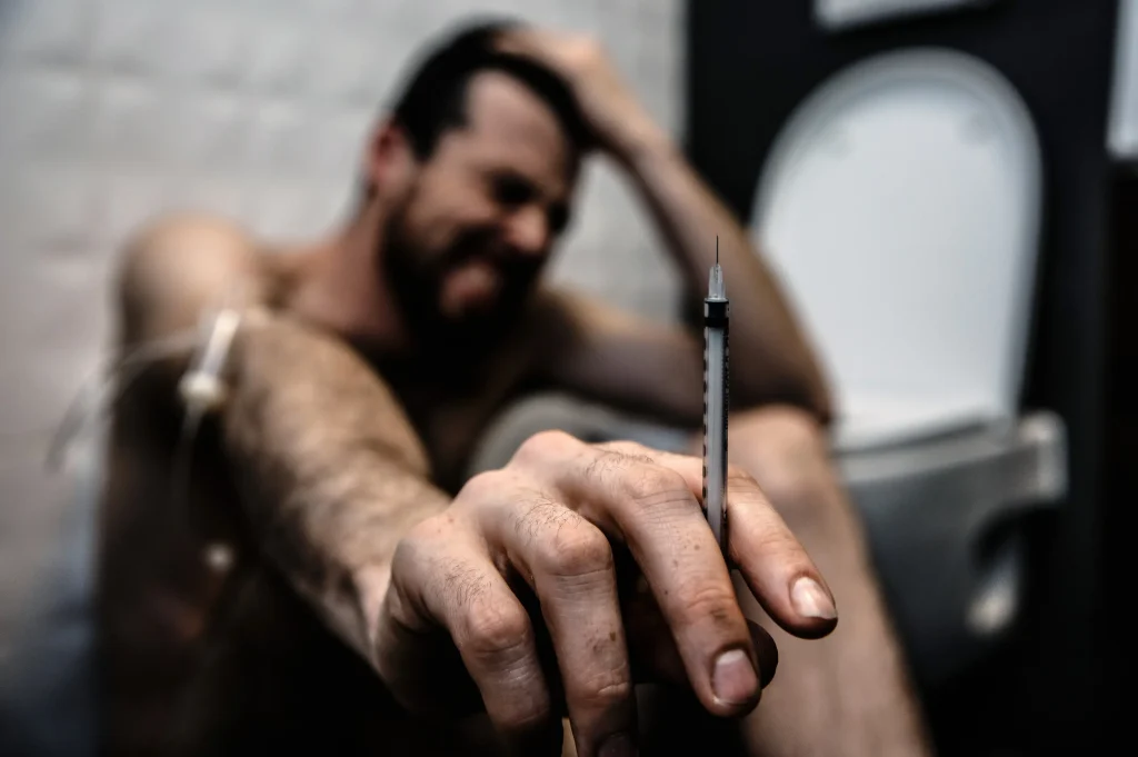man sitting on floor holding syringe representing the need for bipolar disorder treatments and drug intervention