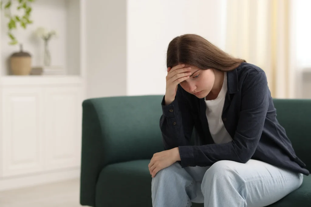 woman sitting on couch holding her head experiencing detox symptoms during recovery