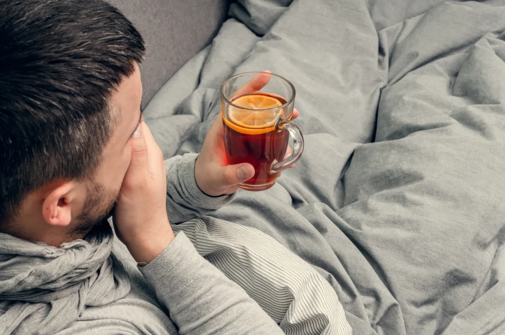 man lying in bed with headache and tea while preparing for rehab and managing discomfort