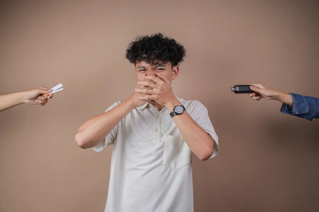 young man showing signs you need addiction treatment being pressured with cigarettes and a vape