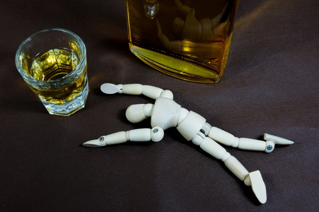 wooden mannequin fallen beside alcohol glass and bottle representing the need for sober living