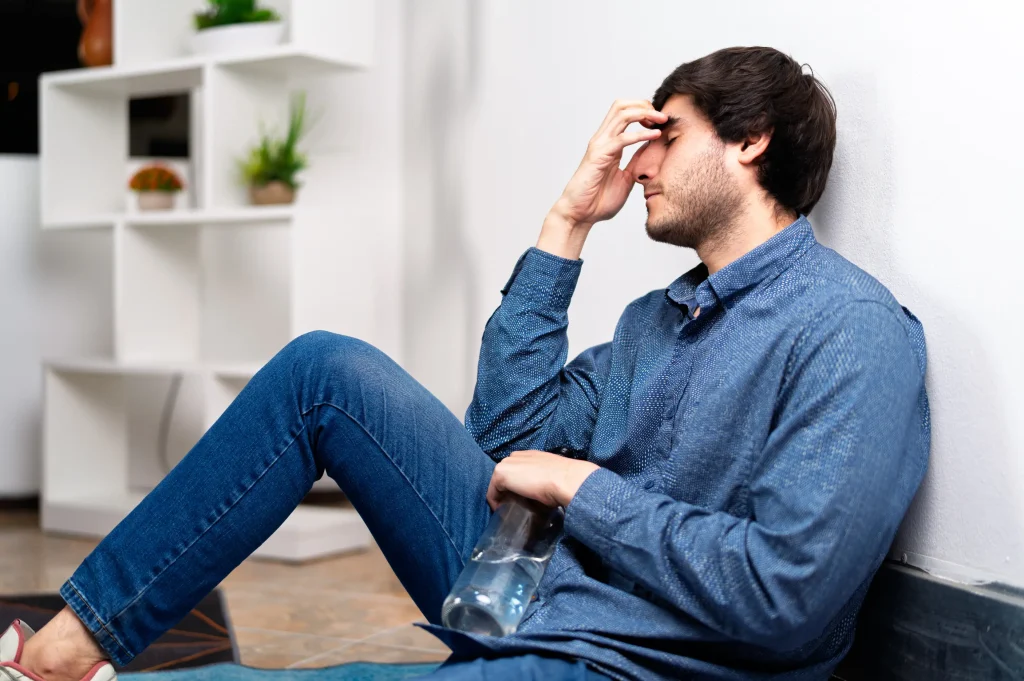 man sitting on floor holding bottle struggling with trauma recovery and alcohol dependence